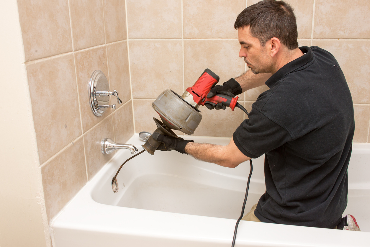 iStock-524026968 how to unclog a sink drain Plumber unclogging a tub drain with an electric auger