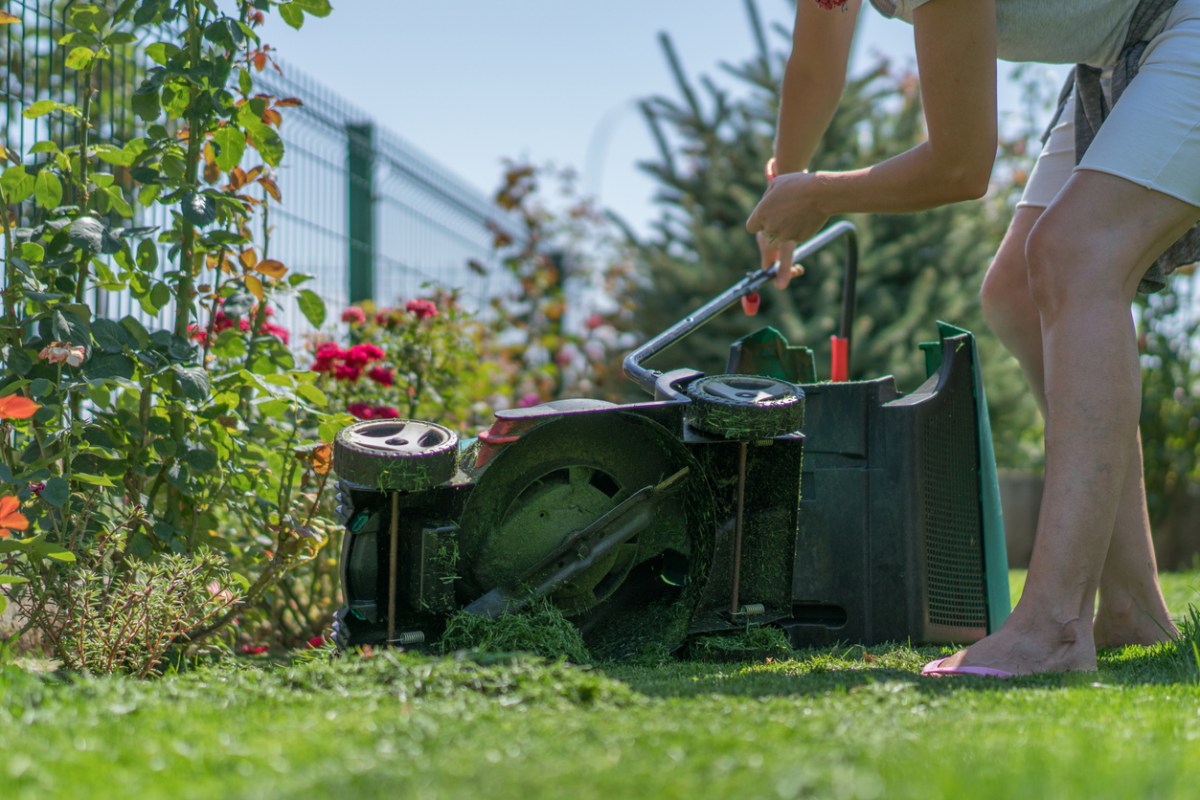 woman examining a broken lawnmower on its side