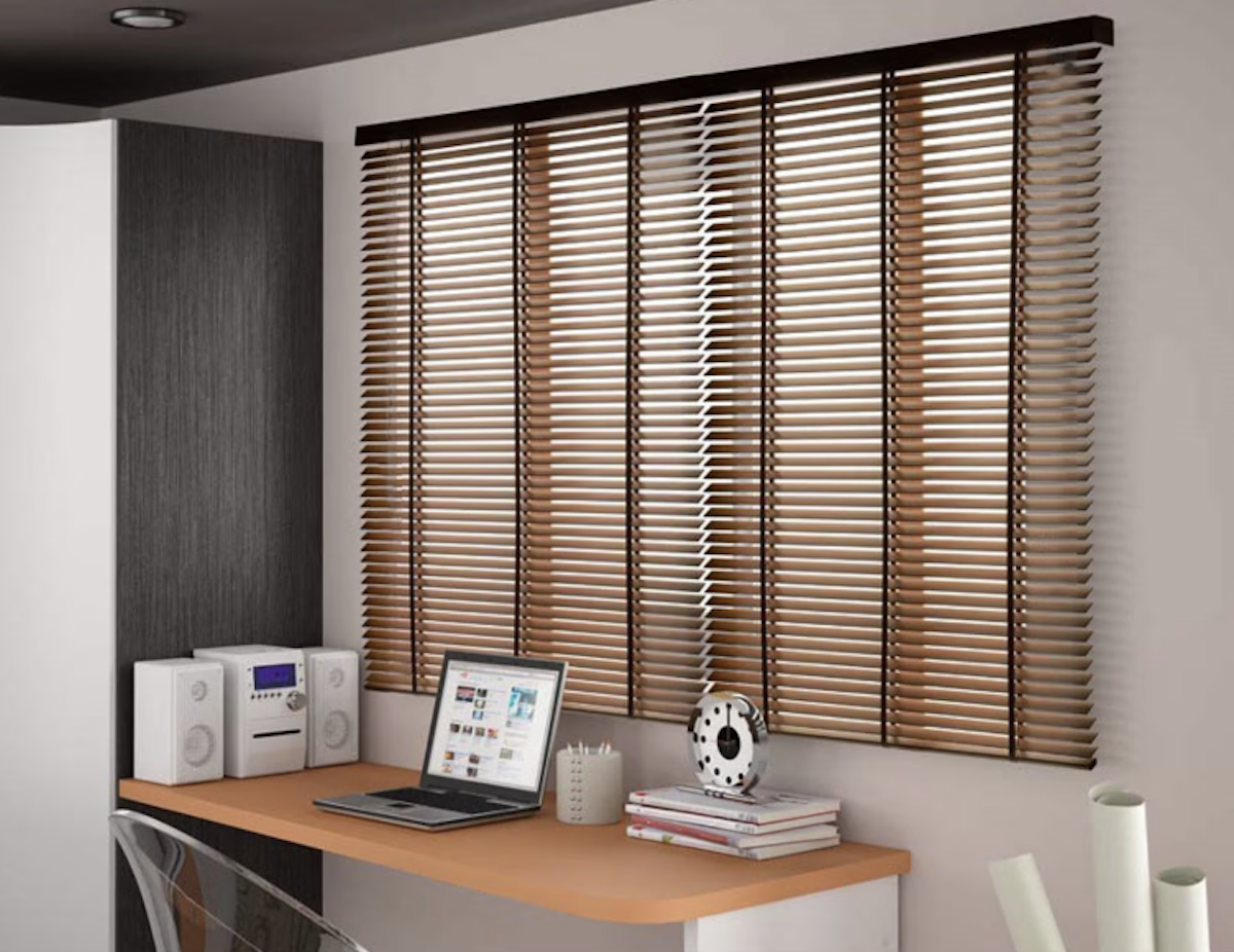 A desk area with dark brown motorized blinds dressing the window above the table top. 