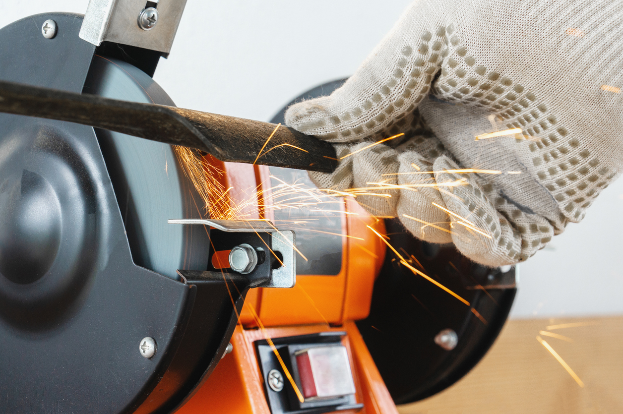 Person wearing gloves sharpening a lawn mower blade