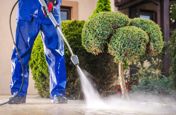 close up of a man in blue overalls pressure washing pavement