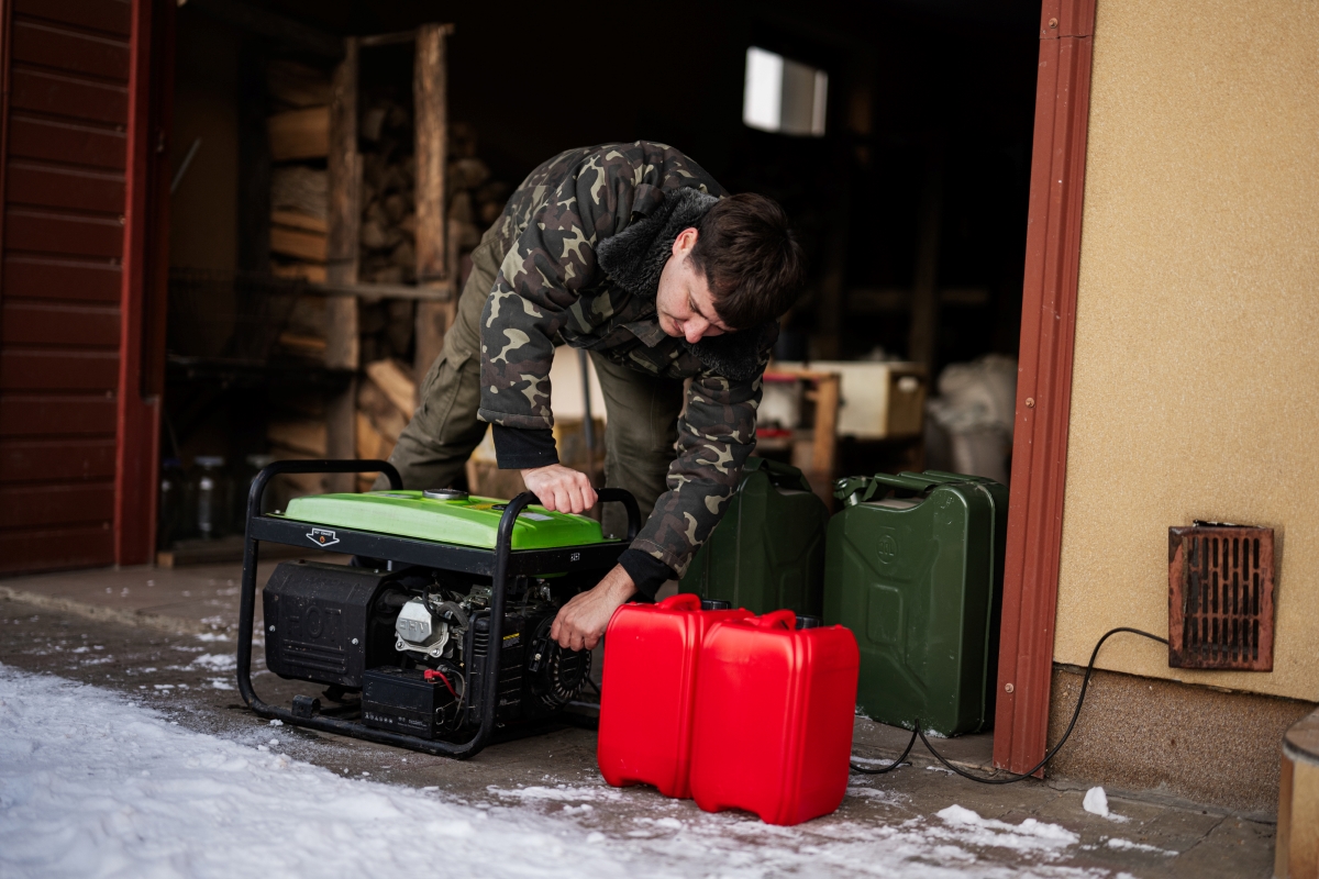 A person is starting a portable home generator next to a fuel can.