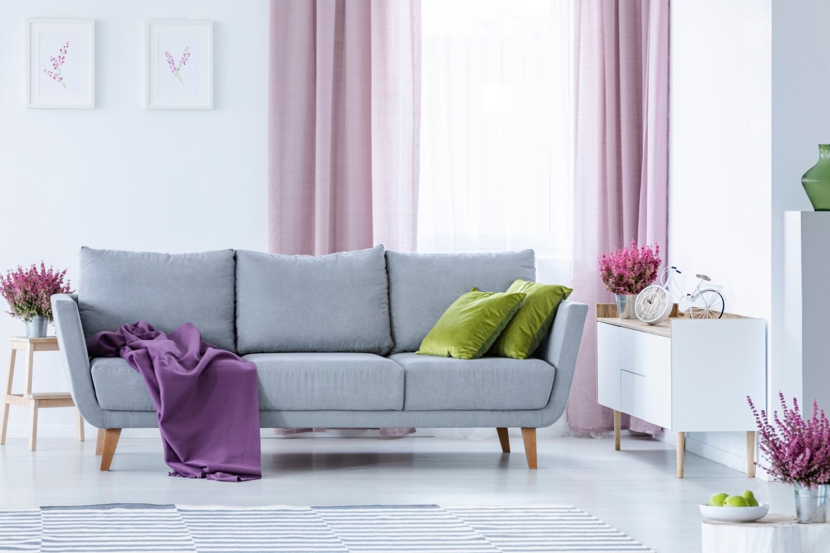 Gray couch with a purple throw blanket and green pillows in front of pink living room curtains