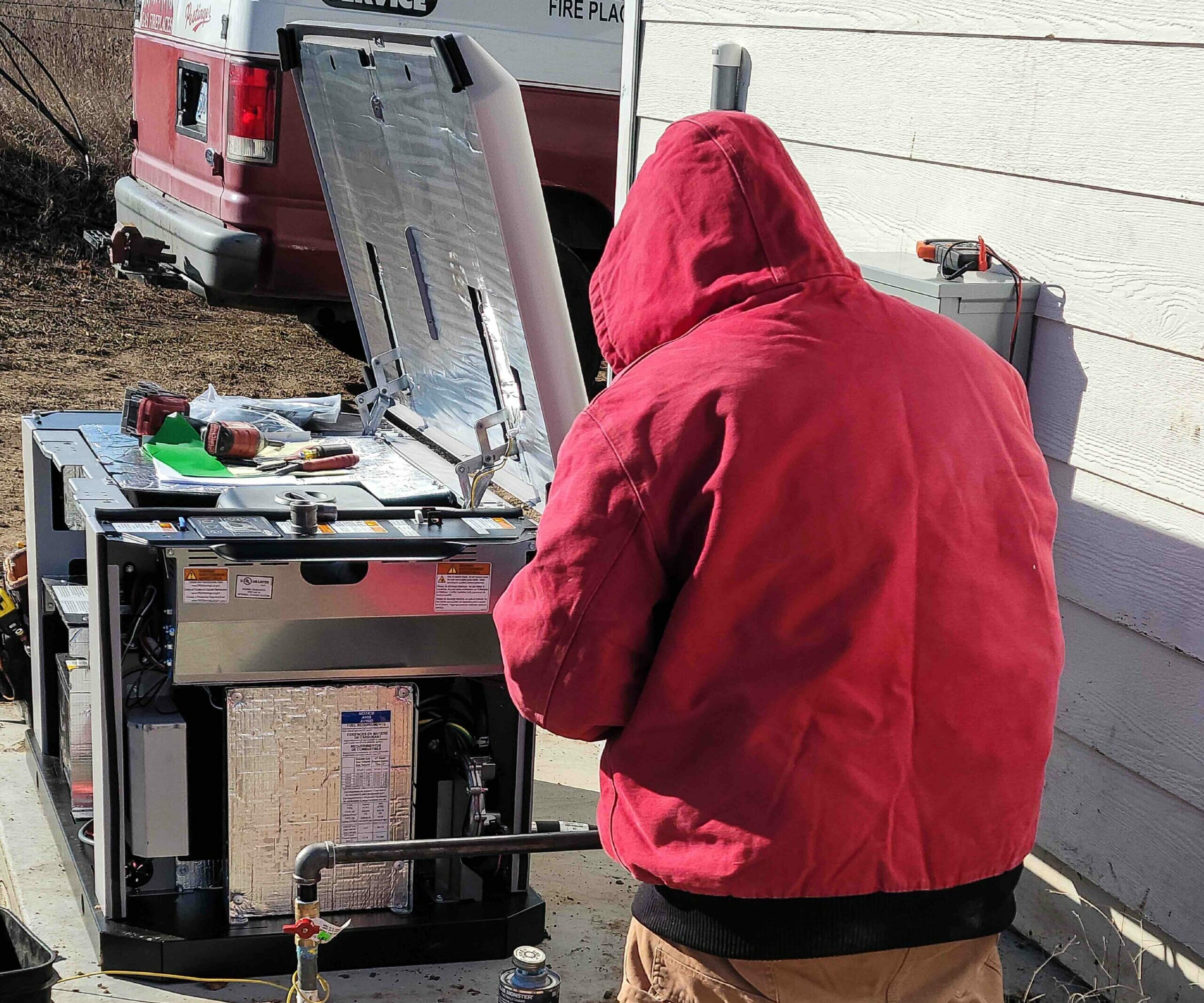 Back view of a man in a red hoodie repairing a residential generator