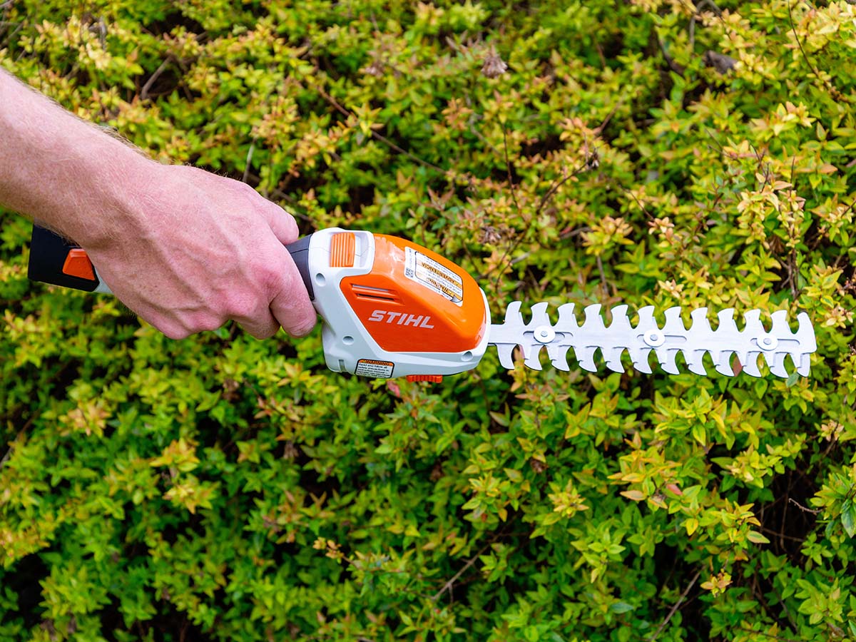The Stihl cordless garden shears with attached hedge trimmer next to a hedge