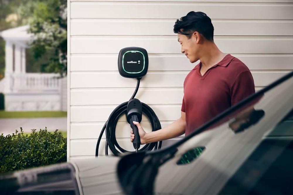 A person removing the best home EV charger from its wall plug to charge a car