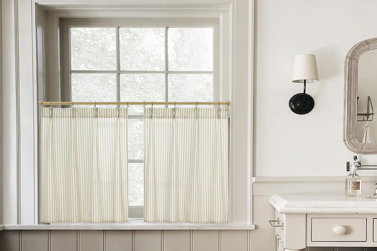 Tan and white apron curtains, which extend a few inches lower than a bathroom window.