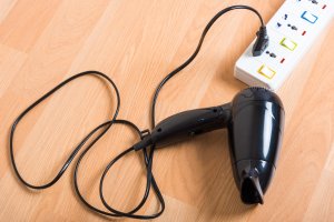 A black hair dryer plugged into a white socket electric power strip.
