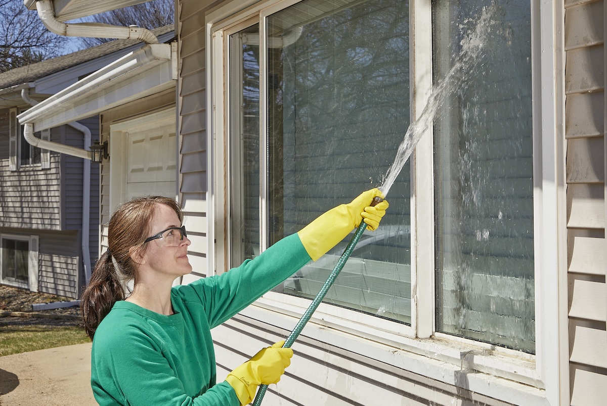 The woman uses a garden hose to rinse the outer windows.