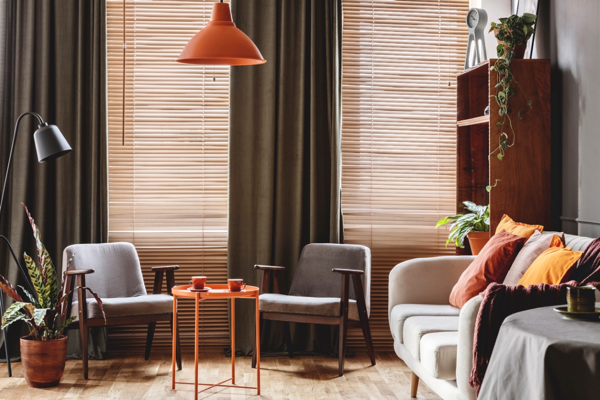 Grey armchair at orange table with drapes and blinds