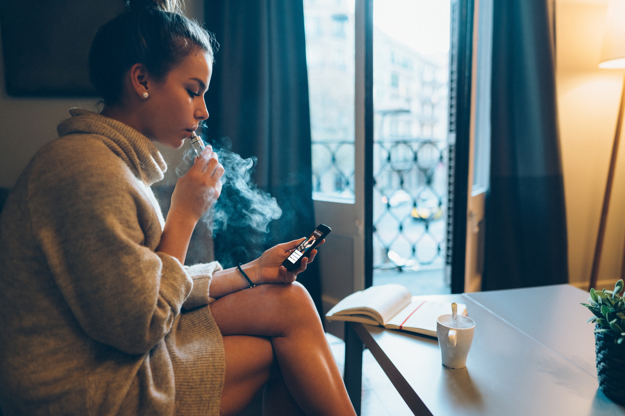 woman smoking indoors while looking at phone