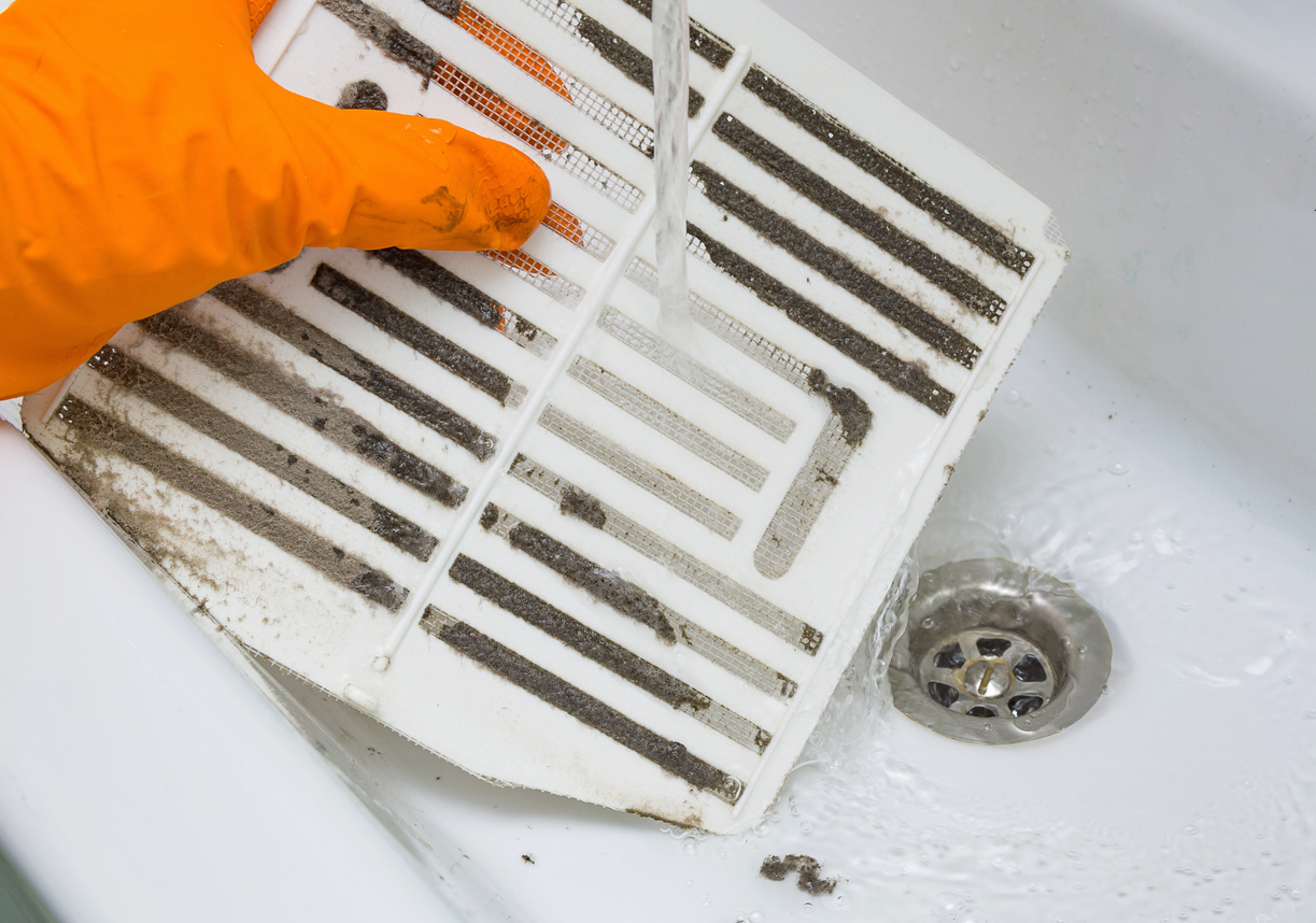 Person in a protective orange rubber glove washes in the sink air filter of the ventilation return duct blocked by dust and debris