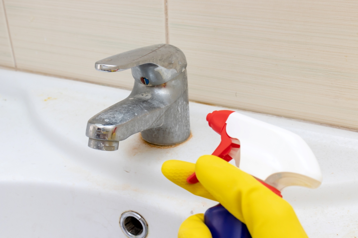 uses for hydrogen peroxide - gloved hand spraying rust on sink faucet