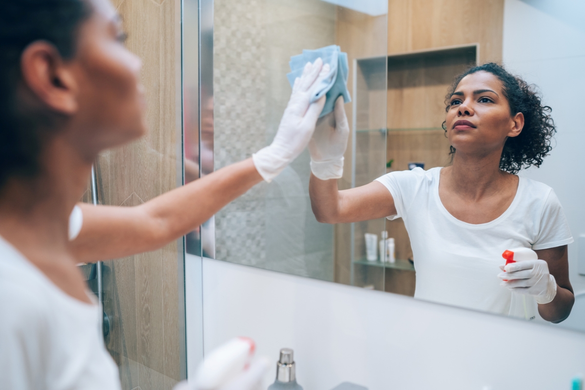uses for hydrogen peroxide - woman using spray cleaner on mirror