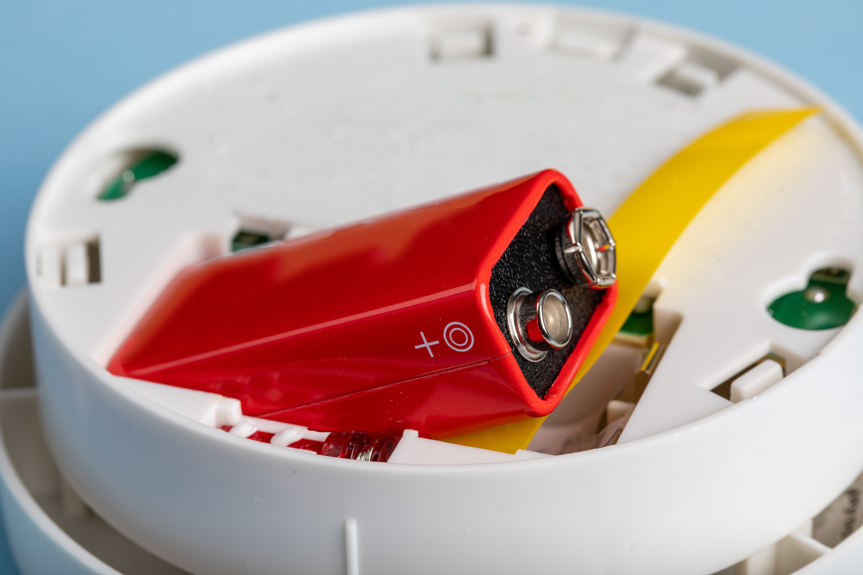 A smoke and fire detector showing the battery being installed