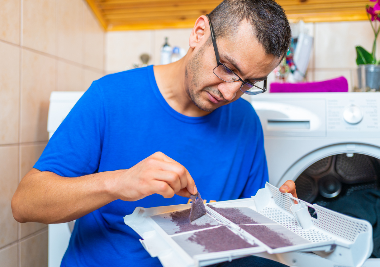 young man is removing lint from fluff dust filter of the tumble dryer