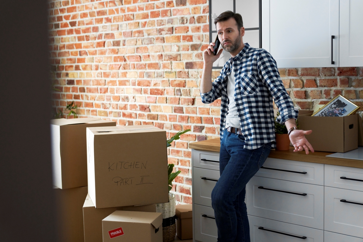 Displeased man talking on phone among moving boxes