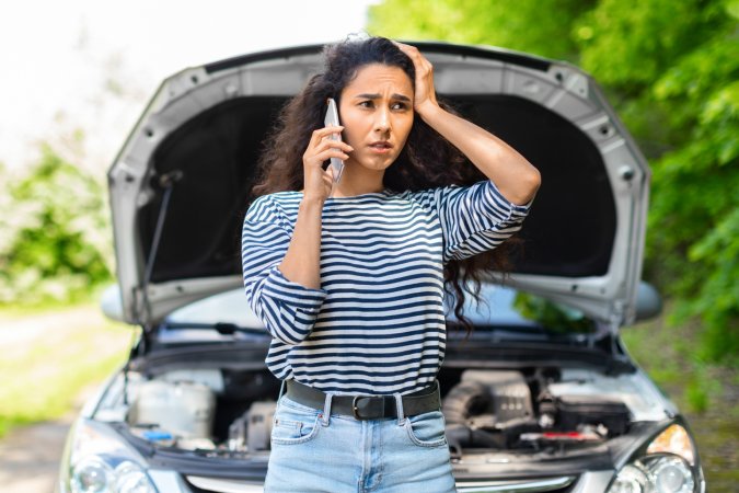 Nervous woman with open car hood calling auto service