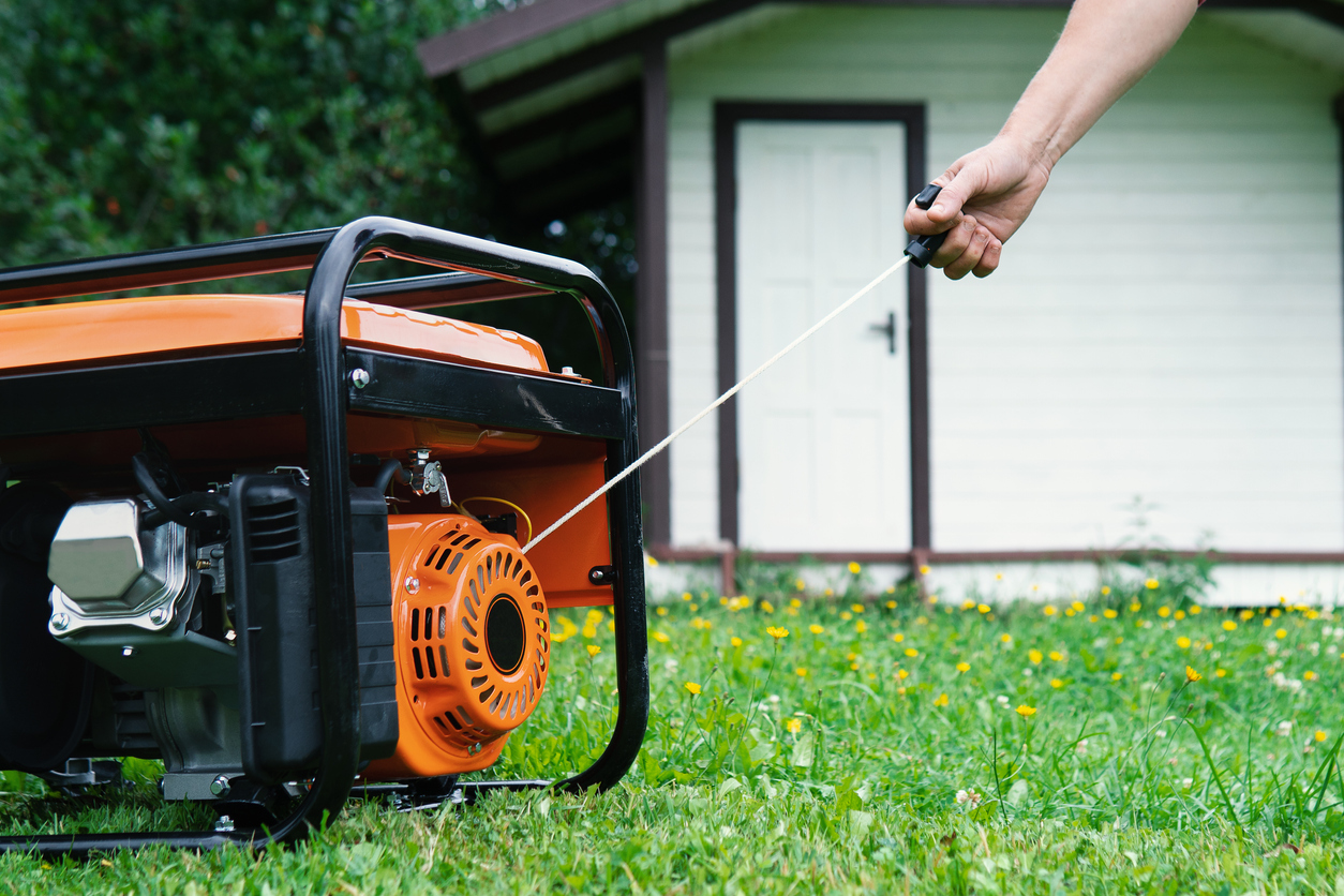 Hand starts a portable electric generator in front of a summer house