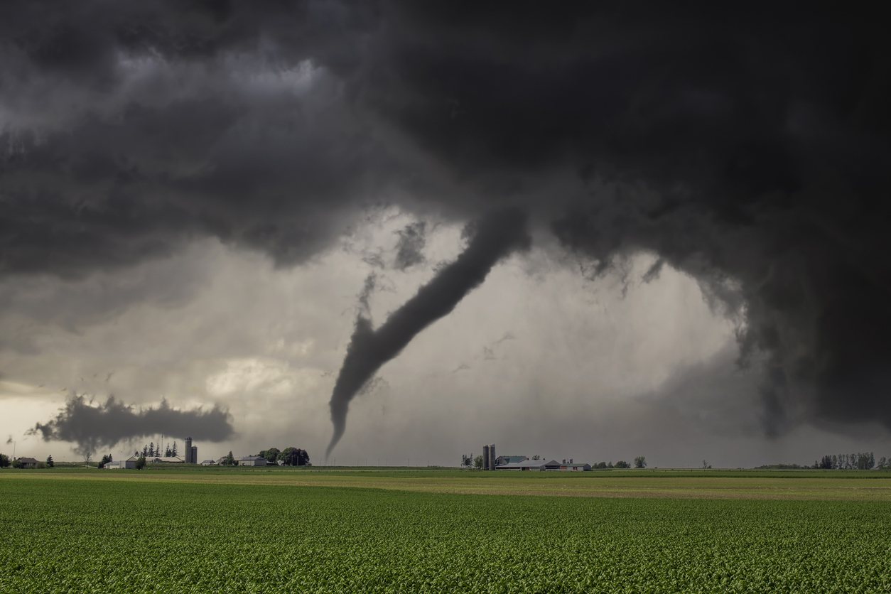 Dark, powerful tornado surrounded by storm clouds touching down over a field.