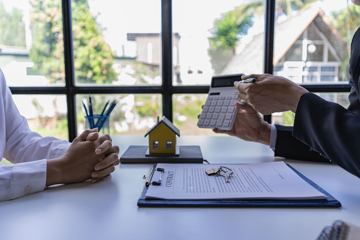 man holding calculator out to show someone else with house on the table illustrating real estate concept