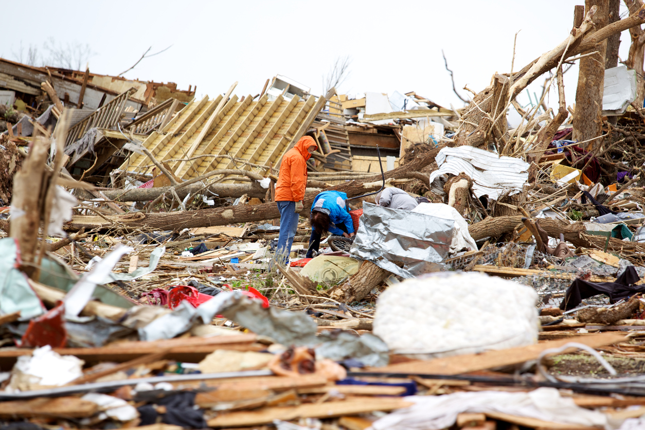Two men searching through debris after a tornado.