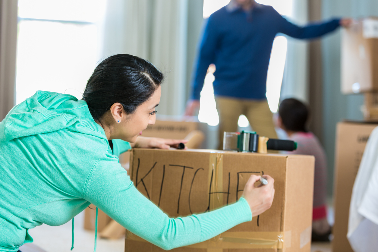 woman in living room writing the word "kitchen" on a cardboard box getting ready to move