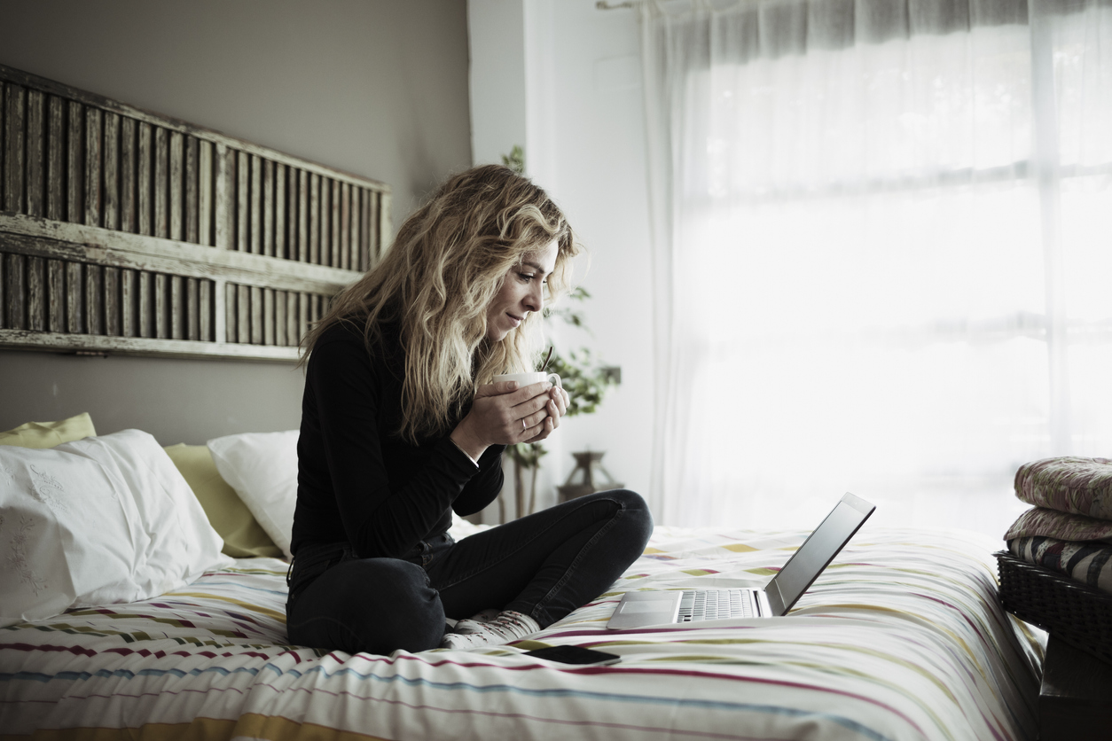 Woman using laptop computer sitting on bed at home