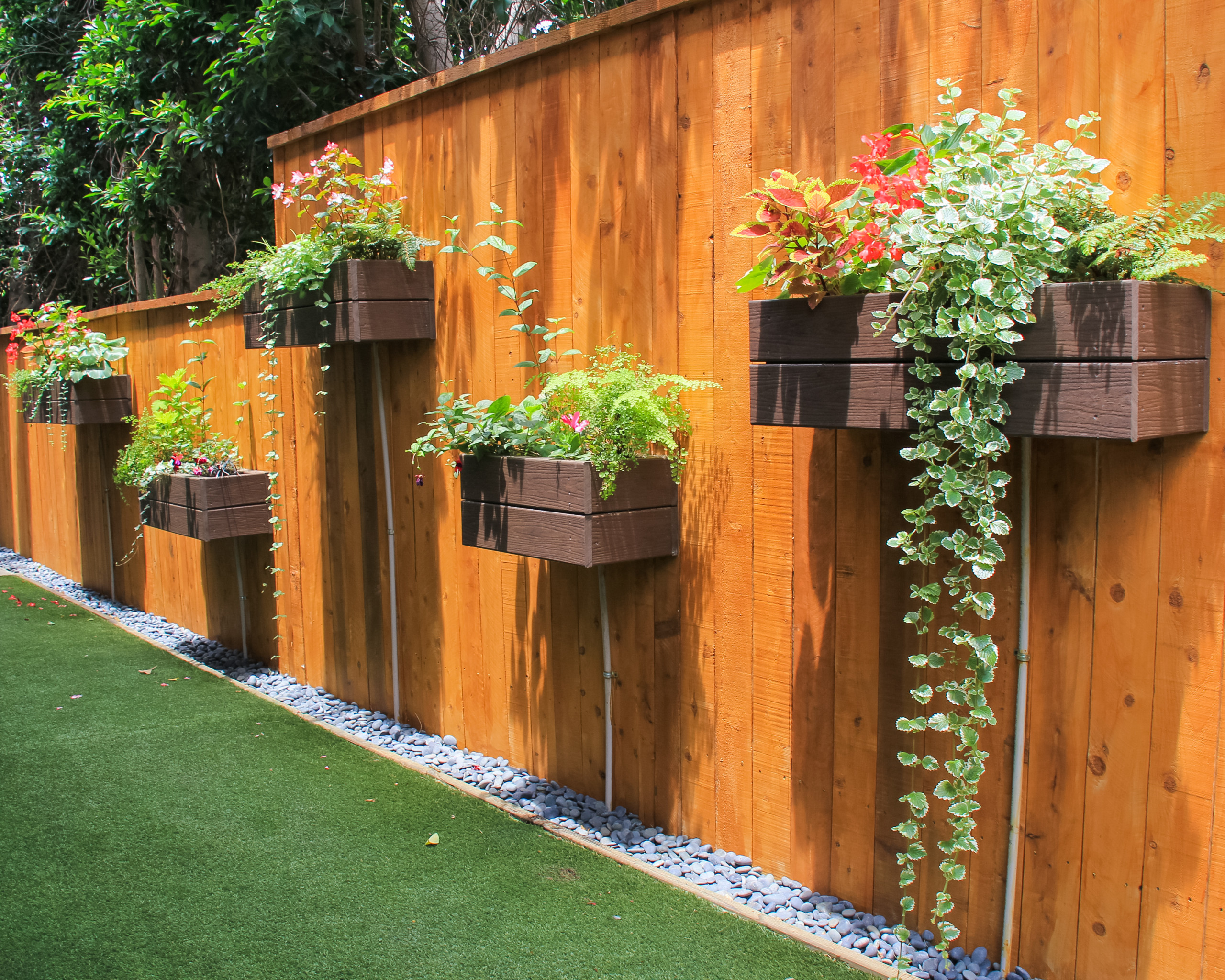 astroturf yard with tall wood fence mounted with box planters filled with beautiful flowering plants