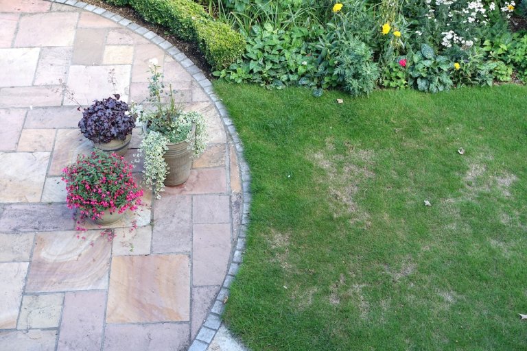 A stone patio with flower pots located next to a lawn with brown, patchy grass.