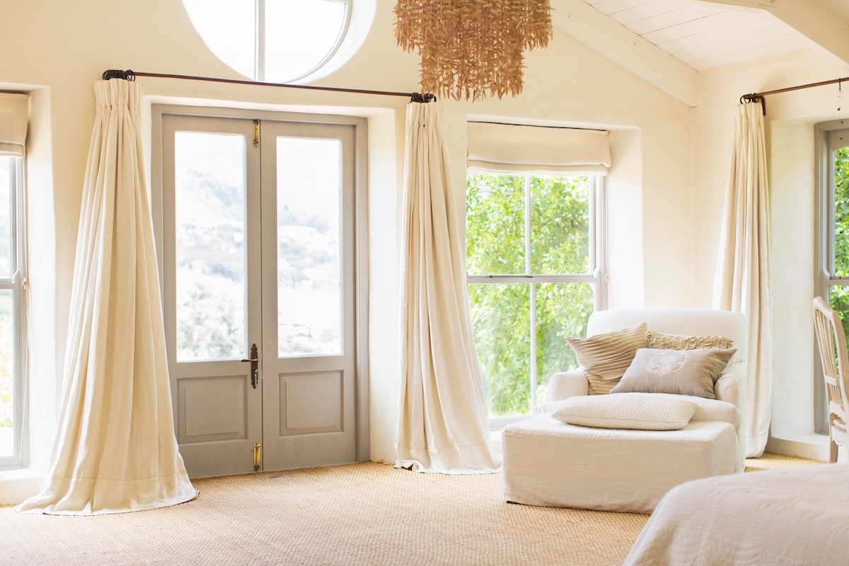 A formal living room with extra long cream-colored curtains on the windows.