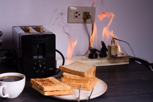 Toaster plugged into an electrical outlet that has caught fire. Toast and coffee in the foreground.