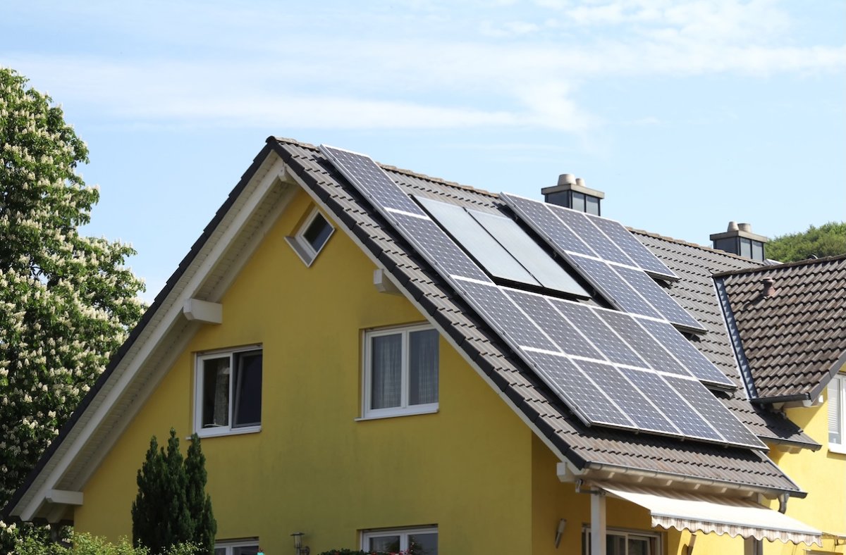 Yellow house with a black roof and solar panels and the roof.