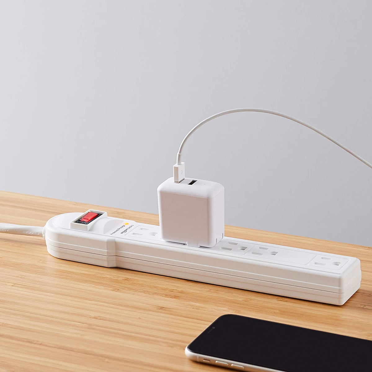 Product photo of an Amazon Basics surge protector with a phone charger plugged into it
