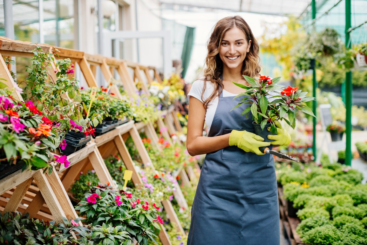 A person in a greenhouse holding a plant while wearing the best gardening apron option