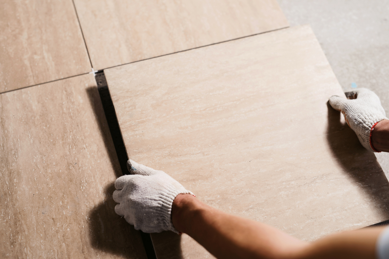 Gloved hands installing ceramic tile flooring