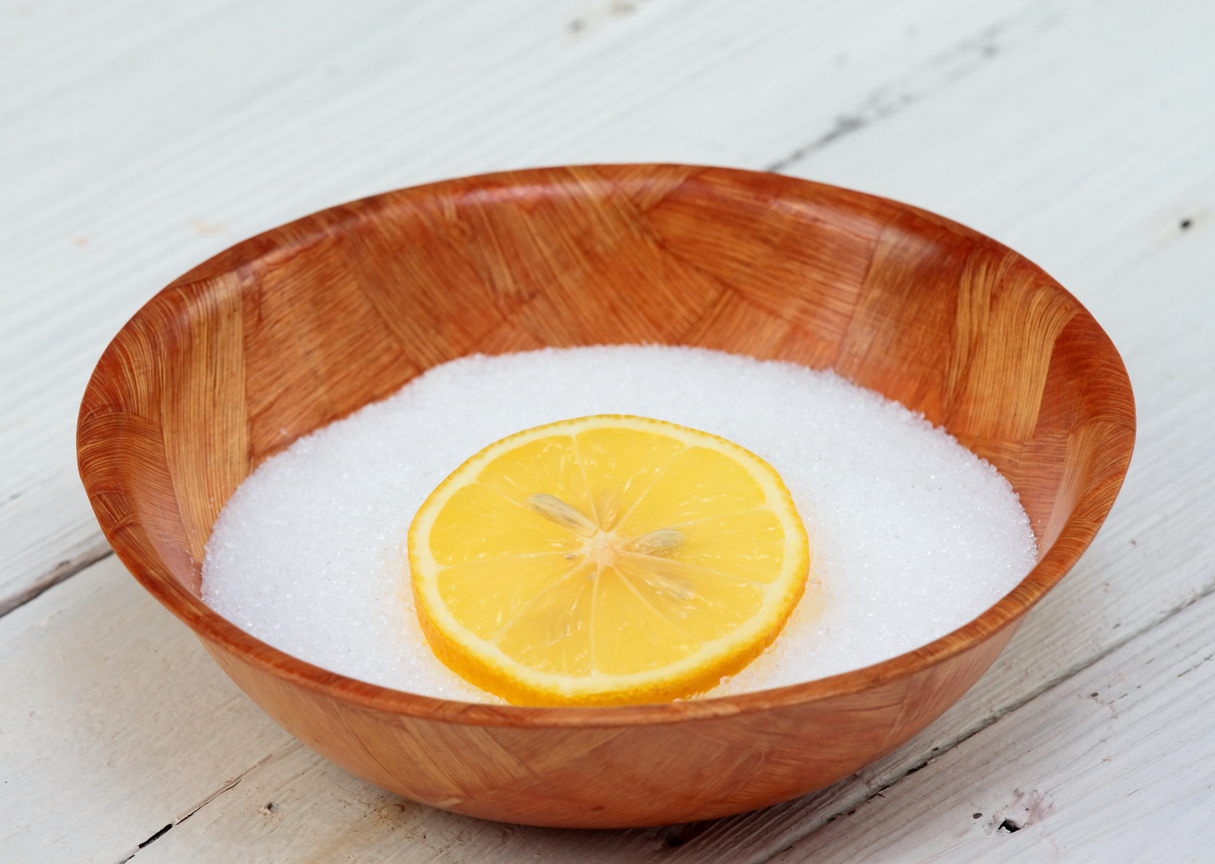 Citric acid powder topped with a lemon slice in a clean wooden bowl