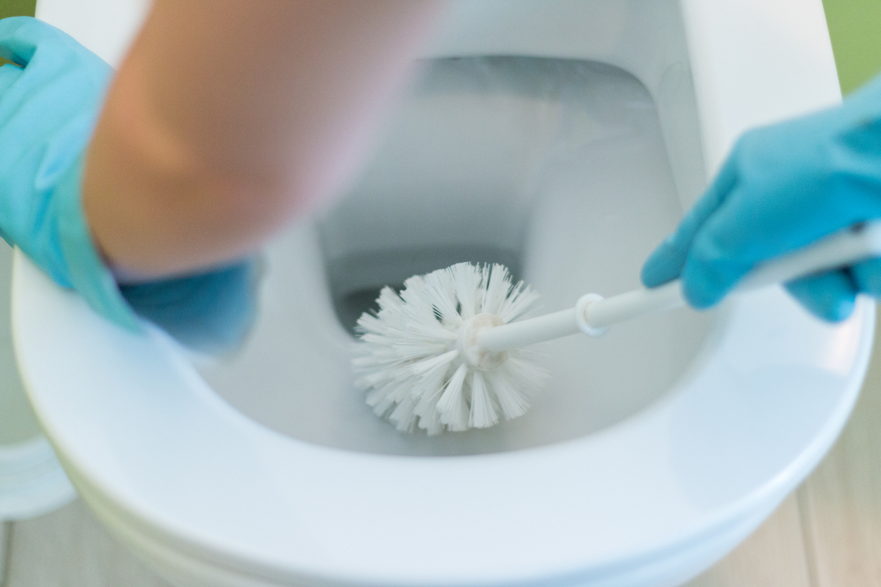 Gloved hands cleaning a toilet bowl with a toilet brush