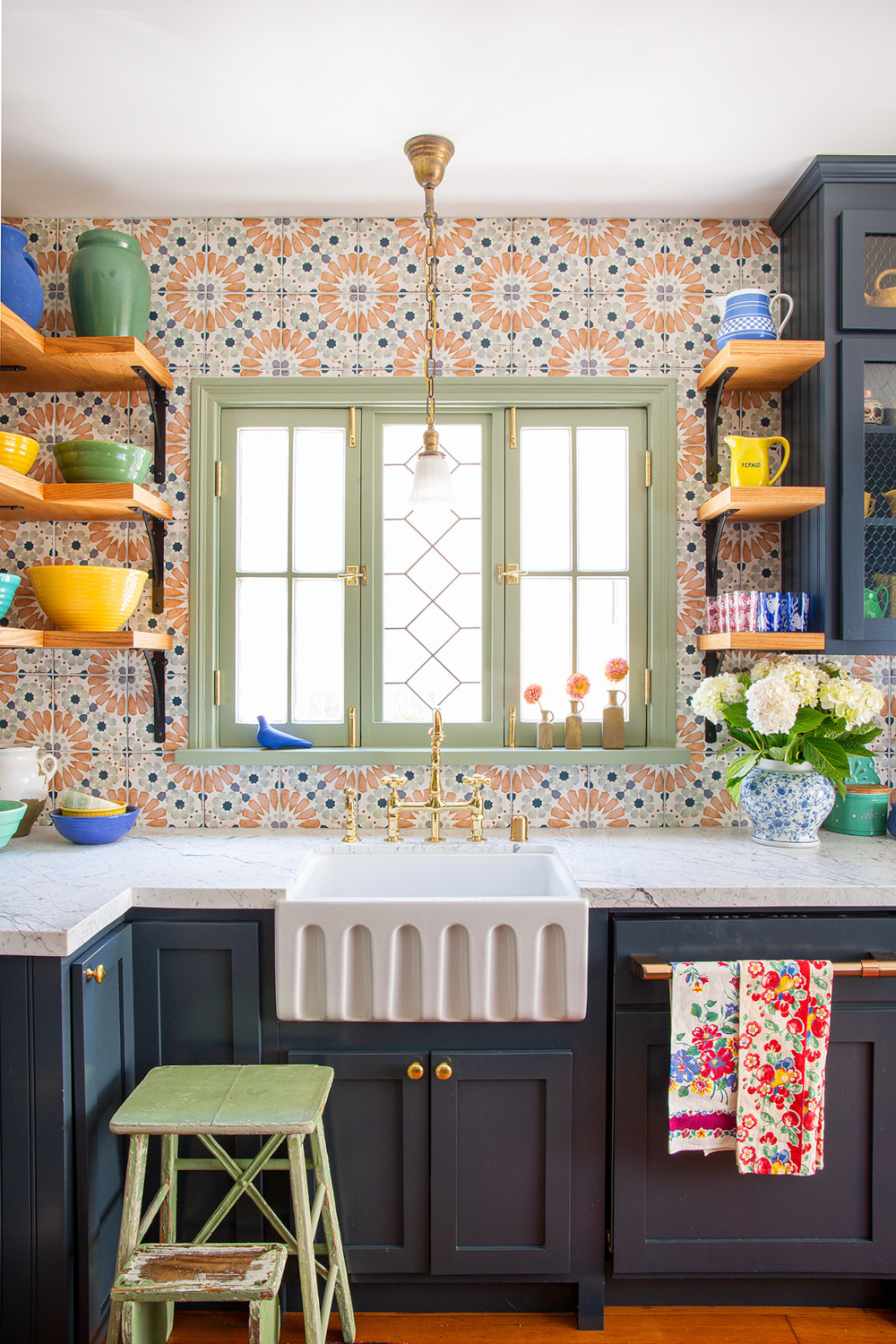 Colorful orange, blue, and white kitchen backsplash accented by a light-green window and dark-blue cabinetry