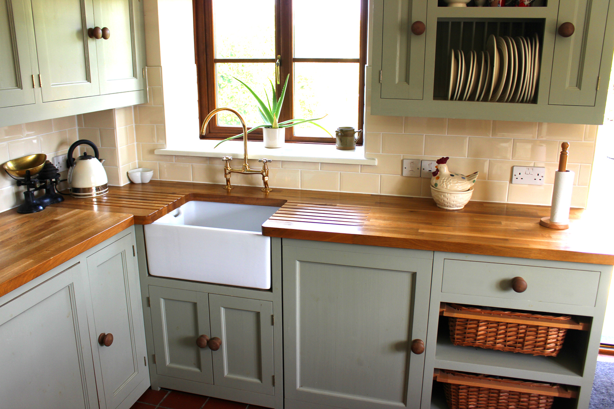 Modern farmhouse-style kitchen with butcher block countertops, green and blue cabinetry, and a cream tile backsplash
