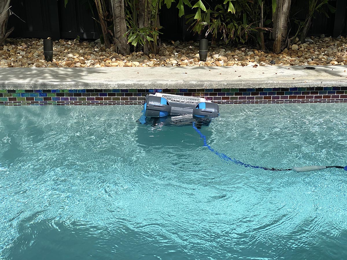 Dolphin Premier Robotic Pool Cleaner moving through pool with deck and rock landscape
