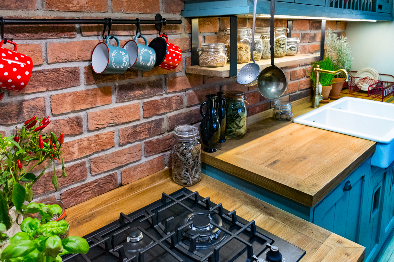 Butcher block countertops with an exposed brick backsplash, fresh herbs, and hanging mugs and utensils