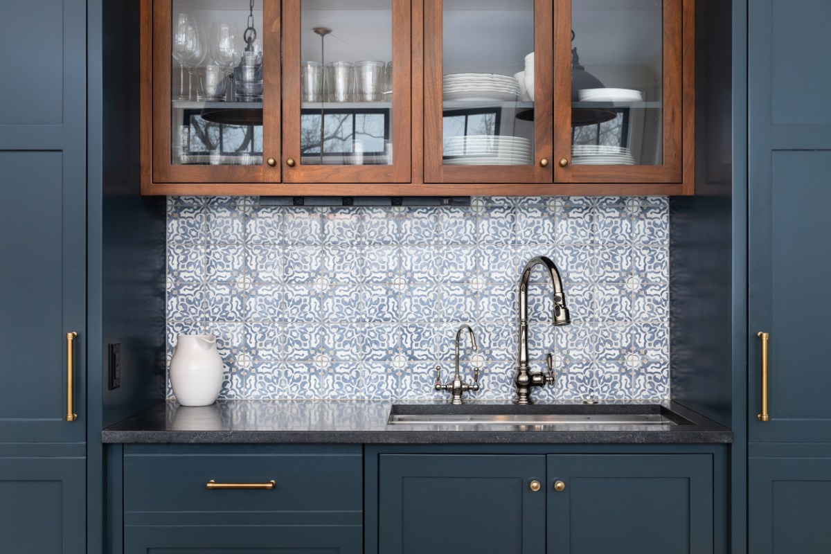 Blue-and-white mosaic tile kitchen backsplash behind a sink and dark-blue cabinets