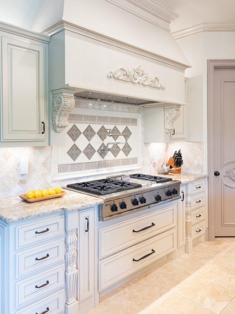 Ornate custom silver-and-white backsplash panel installed behind a gas stove in a white kitchen