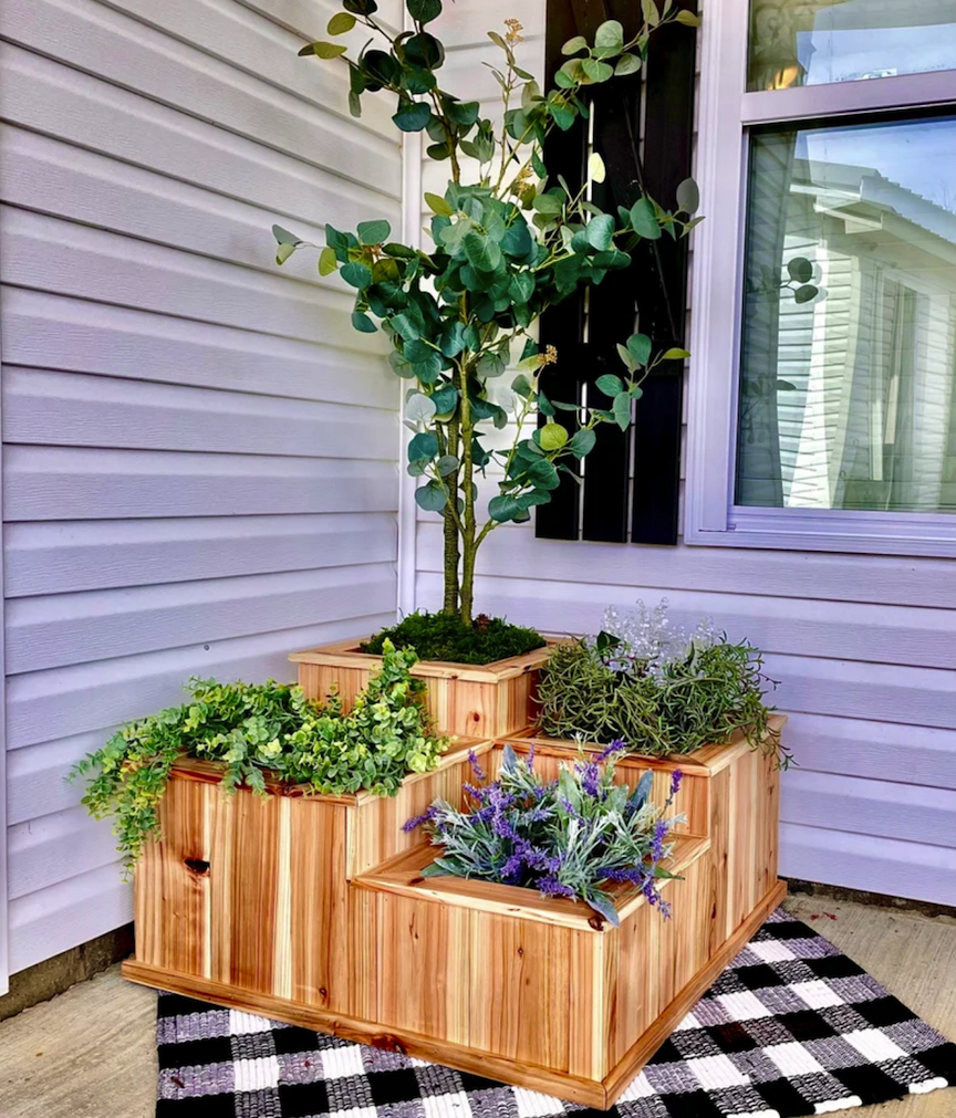 front porch of house with white siding with a large square planter box with tiered sections with one small tree planted in the corner