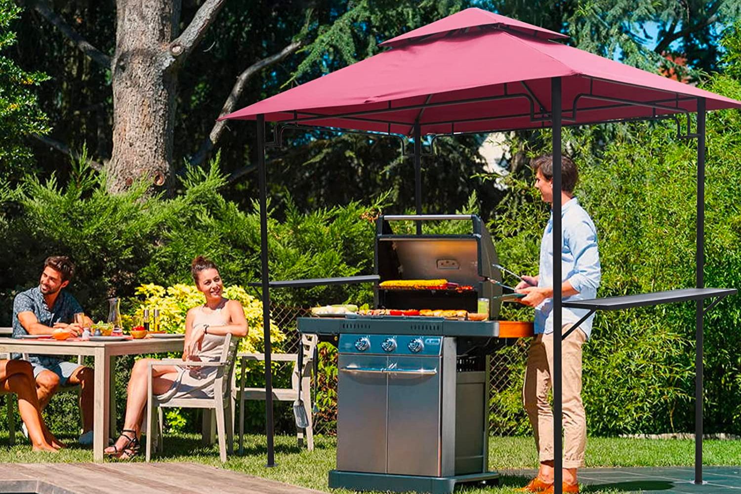 A man and woman outside with one sitting comfortably at a table and the other grilling in the shade under the best grill gazebo option