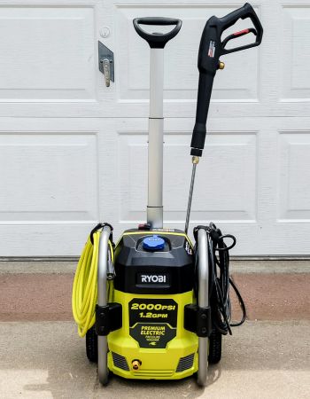 The Ryobi pressure washer 2000 PSI in front of a garage door with all onboard tools and cords neatly stored