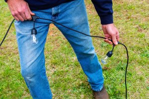 Man stretching out solar string lights cord on grass lawn