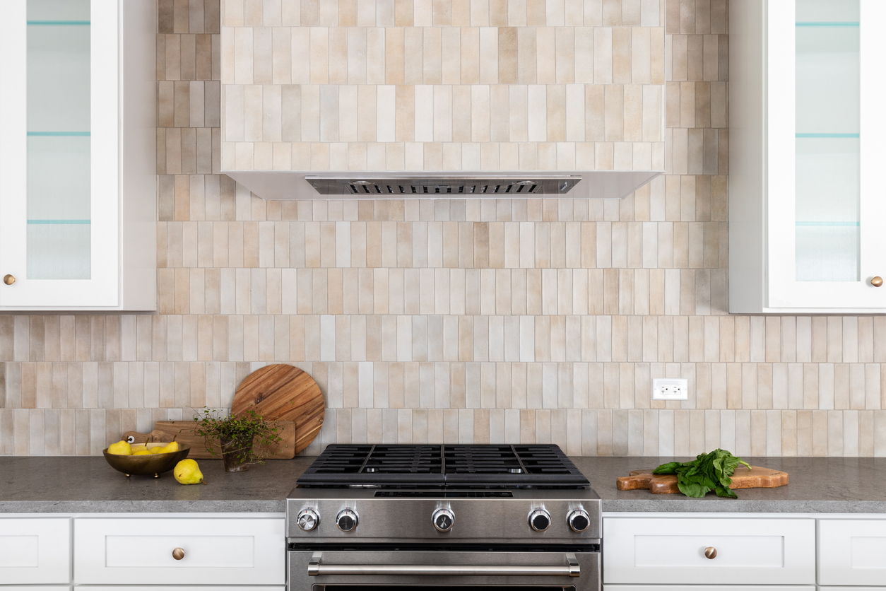 Bright kitchen with a backsplash made of small white, tan, and light gray vertical tiles that extend up the range hood