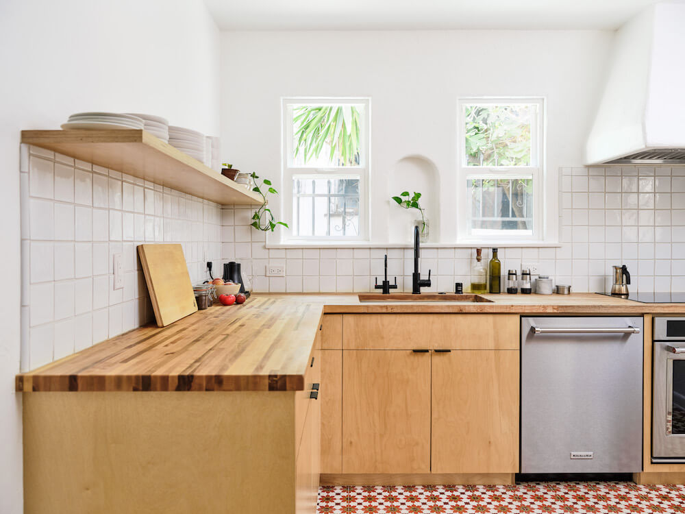 Bright Scandinavian-style kitchen with a white tile backsplash and light wood countertops, cabinets, and shelving